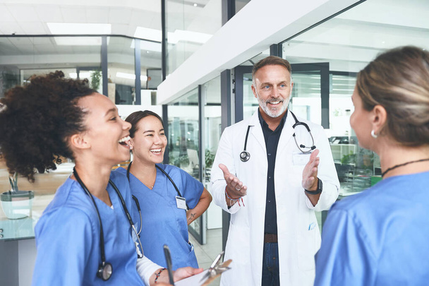 Αυτή είναι η αστεία της παρέας. ένας όμορφος ώριμος γιατρός που στέκεται με τις νοσοκόμες του και συζητάει στην κλινική - Φωτογραφία, εικόνα