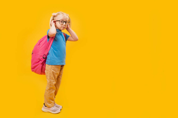 Studio full length ritratto con sfondo giallo di piccola ragazza bionda caucasica che indossa lo zaino per la scuola. Copia spazio. - Foto, immagini