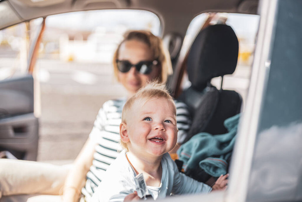 Mutter und ihr Baby auf Sommerreise mit der Familie, auf dem Beifahrersitz sitzend, im Auto auf den Fahrkartenkauf des Vaters wartend - Foto, Bild