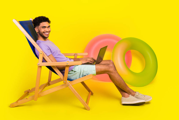 Side cadre of man lying sunbed chair copywriter comfortable freelancer job on beach near rubber rings isolated over yellow color background. - 写真・画像