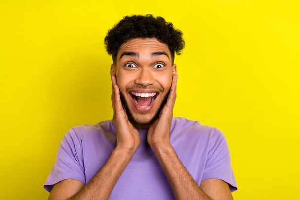 Photo of charming excited man wear violet t-shirt smiling hands cheeks isolated yellow color background. - Fotoğraf, Görsel