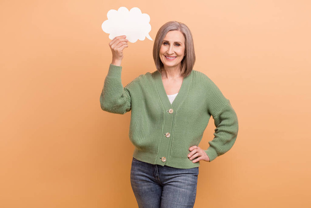 Photo of satisfied old senior business developer woman hold paper bubble cloud her speech message announce isolated on beige color background. - Foto, Imagen