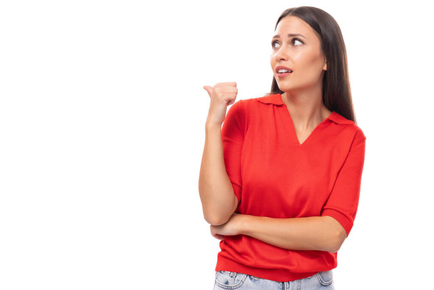 pretty smart caucasian woman with black hair is wearing a red blouse with a halter neckline pointing her finger at the advertising space. - Photo, Image