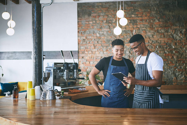 Интернет жужжит об их бренде кофе. двое молодых людей, работающих в кафе с цифровой планшеткой - Фото, изображение