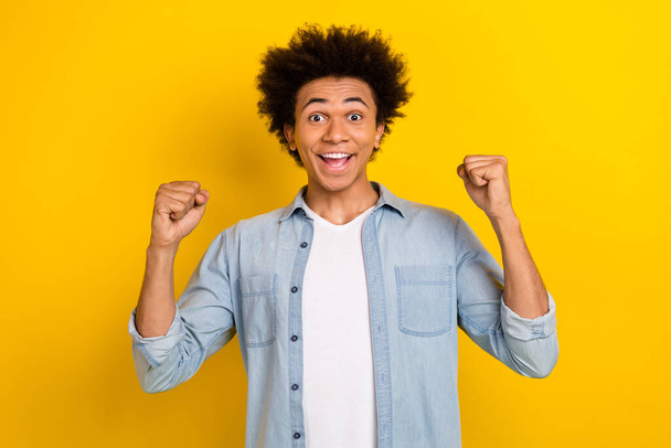 Photo of lucky cool guy dressed denim shirt rising fists screaming yeah yes isolated yellow color background. - Foto, Imagen