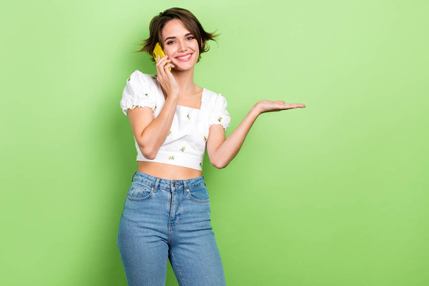 Photo of sweet cute lady wear white crop top speaking modern gadget holding arm empty space isolated green color background. - Foto, imagen