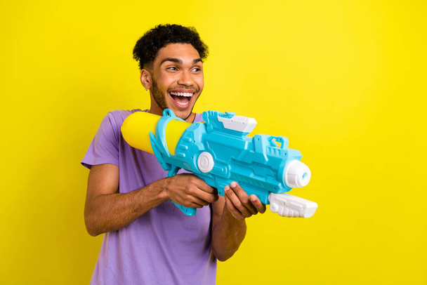 Photo of carefree positive person hands hold water gun pistol look empty space isolated on yellow color background. - Foto, afbeelding