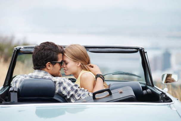 Getting close and sharing a moment. An attractive young couple in their convertible while on a roadtrip - Photo, image