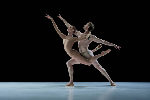 Talented, artistic young couple, man and woman, ballet dancers making impressive performance against black studio background. Concept of beauty, classical dance style, inspiration, movements. Ad - Foto, afbeelding