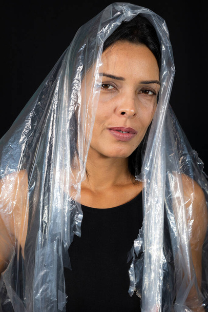 ベールの形で彼女の頭の上にビニール袋を持つ女性。プラスチックの使用に対する抗議。環境問題。黒の背景に隔離された. - 写真・画像