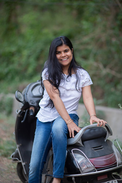 Μια ινδική όμορφη νεαρή κοπέλα με σκούτερ χαμογελώντας και διασκεδάζοντας - Φωτογραφία, εικόνα