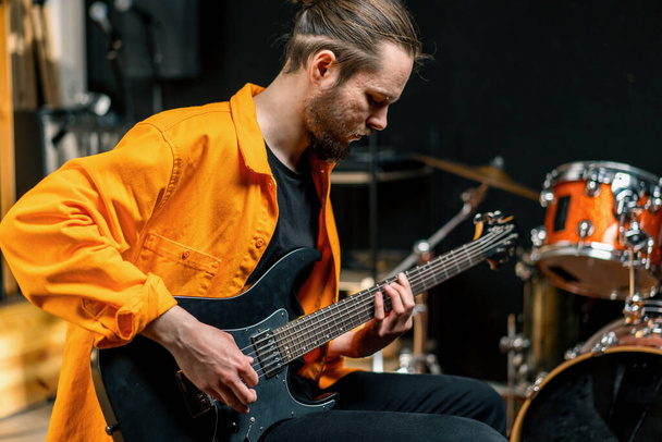 portrét mladého rockového umělce s elektrickou kytarou v nahrávacím studiu hrající vlastní skladbu hudební nástroje bicí pozadí - Fotografie, Obrázek