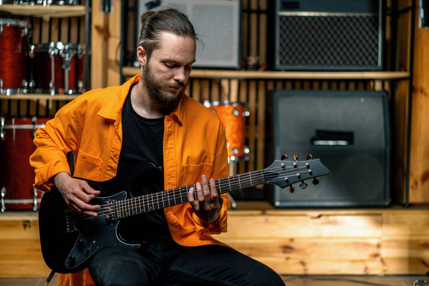 portret młodego artysty rockowego z gitarą elektryczną w studiu nagraniowym grającego własny utwór muzyczny perkusja tło - Zdjęcie, obraz