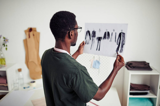 Молодой черный модельер держит в руках лист скечей для новой коллекции, которую он создал - Фото, изображение