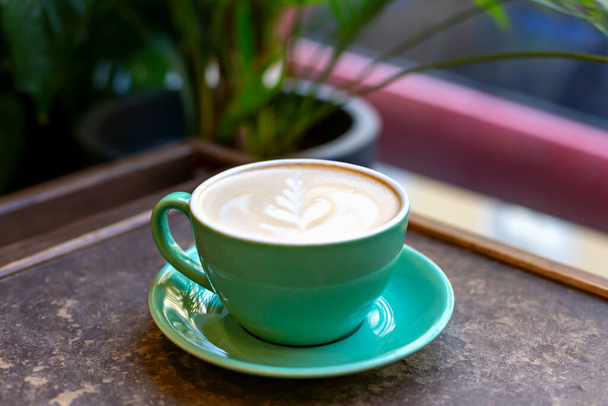 テーブルの上の緑のセラミックカップのパターンを持つ新鮮なおいしい香りのコーヒーラテを閉じます。選択的焦点 - 写真・画像