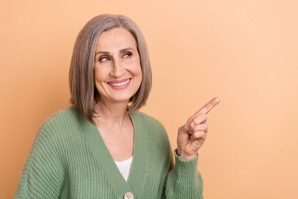 Photo of retired business lady wear trendy cardigan direct finger mockup looking interested news template isolated on beige color background. - 写真・画像