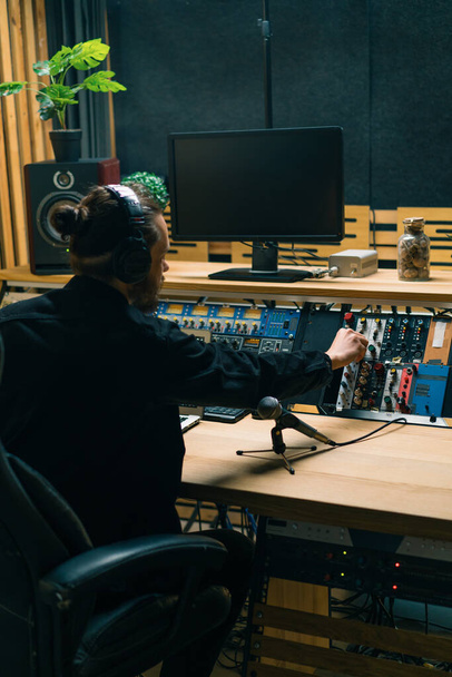 jeune ingénieur du son avec écouteurs travaillant dans un studio de musique avec moniteurs et un égaliseur mélangeant des pistes de mastering - Photo, image