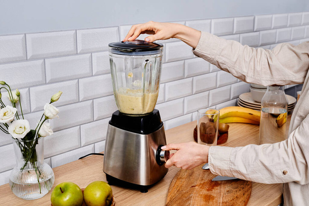 Nahaufnahme einer Frau, die in der Küche im Mixer frischen Saft aus Früchten herstellt - Foto, Bild