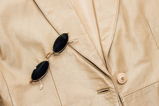 Gold-rimmed sunglasses on the texture of a brown leather jacket, genuine soft leather. - Photo, Image