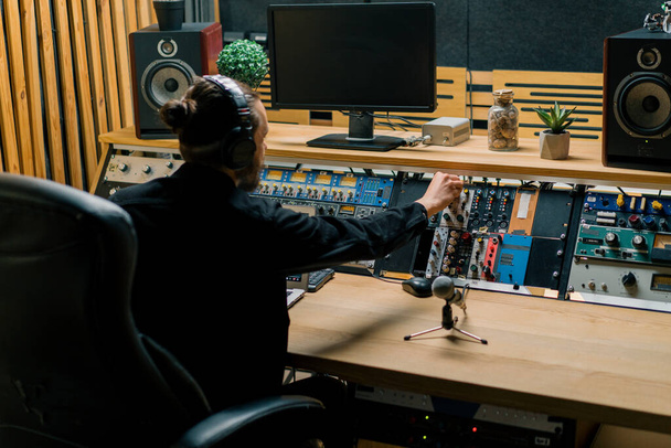 joven ingeniero de sonido con auriculares trabajando en un estudio de música con monitores y un ecualizador mezclando pistas de masterización - Foto, Imagen