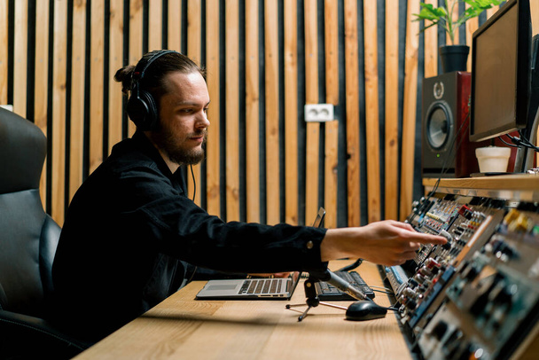 молодий звукорежисер з навушниками, що працюють у музичній студії з моніторами та еквалайзерним змішуванням мастерингу треків - Фото, зображення