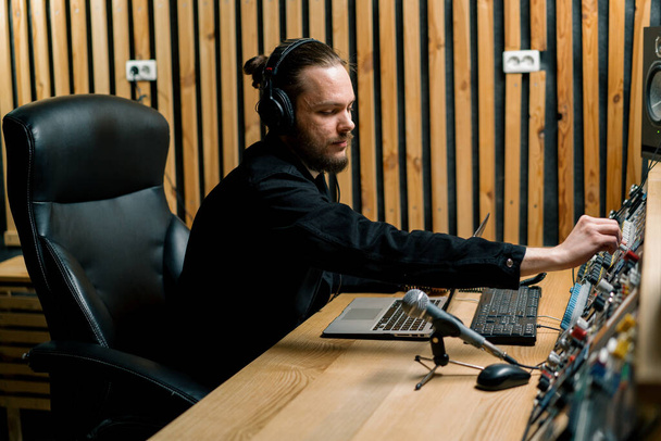 young sound engineer with headphones working in a music studio with monitors and an equalizer mixing mastering tracks - Fotografie, Obrázek