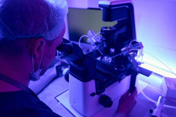 Man laboratory technician adjusting microscope with micromanipulator before working with stem cells or embryos - Photo, image