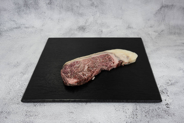 Französisches kulinarisches Stillleben. Stück Wagyu Rinderlende auf einer schwarzen Kacheloberseite. - Foto, Bild