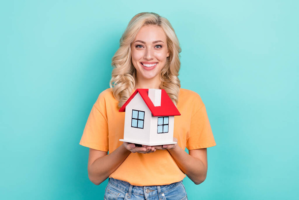 Photo of cheerful charming girl wear orange t-shirt holding small red roof house isolated turquoise color background. - Foto, immagini