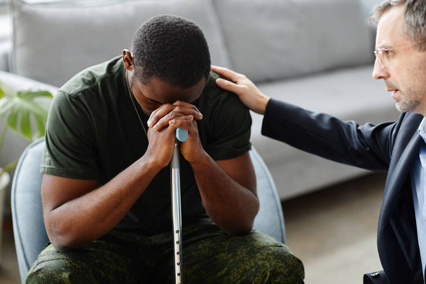 Volwassen psycholoog troosten en ondersteunen van zwarte soldaat tijdens de behandeling van PTSS in therapie sessie - Foto, afbeelding