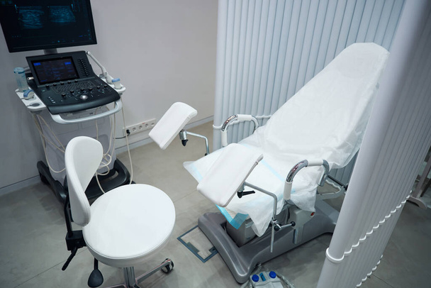 Fotografie gynekologické ordinace, kde je umístěno vybavení pro vyšetření pacientů. Kancelář pro přijímání pacientů s gynekologickou židlí a ultrazvukovým strojem - Fotografie, Obrázek