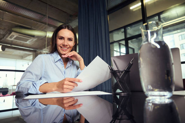 Pas-up portrét radostného firemního pracovníka, sedícího za stolem a držícího v ruce dokument - Fotografie, Obrázek