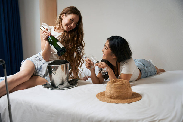 Úgy döntöttek, hogy pezsgővel ünneplik a lánybúcsút az ágyban. Két lány, akik egy hotelszobában ünnepelnek. - Fotó, kép