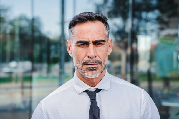 Individual close up portrait of serious mature businessman looking pensive at camera at workplace. Successful handsome corporate male executive ceo standing with confident and toughtful attitude. High - Фото, зображення