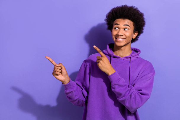 Photo promoter of youngster man chevelure wearing violet hoodie indicating fingers mockup interested brand isolated on purple background. - Фото, изображение