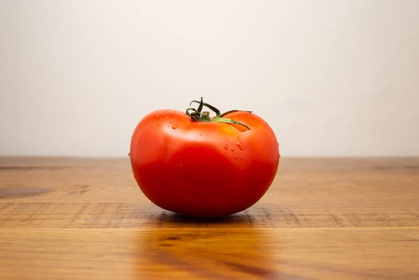 One ripe red tomato on a rustic wooden table, with the neutral white background. - Foto, immagini