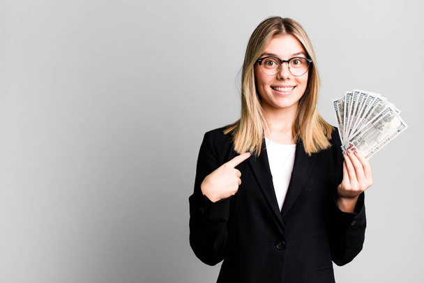 Genç ve güzel bir kadın kendini mutlu hissediyor ve heyecanlı bir şekilde kendini işaret ediyor. iş ve para kavramı - Fotoğraf, Görsel