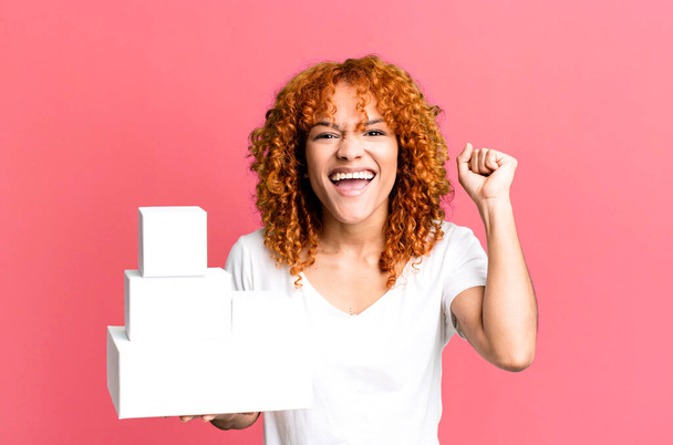cabello rojo bonita mujer sintiéndose sorprendido, riendo y celebrando el éxito. concepto cajas de paquetes en blanco - Foto, imagen
