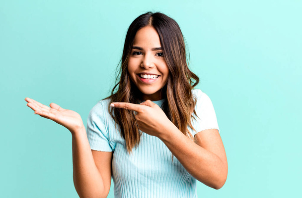 hispanic pretty woman smiling cheerfully and pointing to copy space on palm on the side, showing or advertising an object - 写真・画像