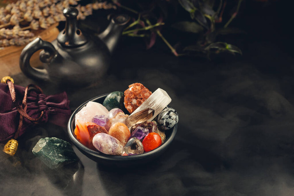 Bunch of Colorful Crystals and Rough Mineral Stones in the Black Bowl Shrouded in a Mystical Mist. Crystal Healing Concept. Copy Space for Text - Foto, afbeelding