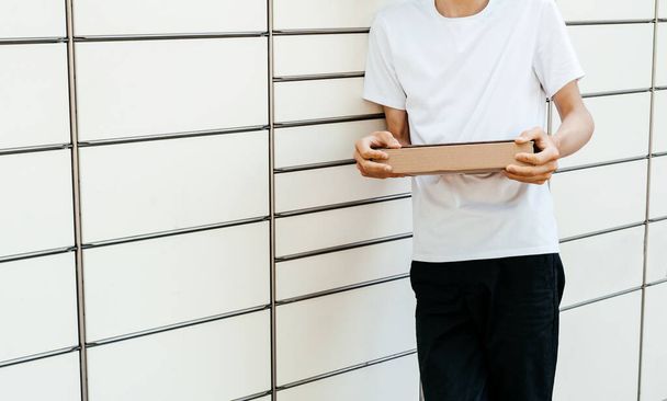 Muž s krabicí v rukou u samoobslužného poštovního terminálu. Stroj na doručování balíků. Osoba držící lepenkovou krabici. Doručení pošty a poštovních služeb, on-line nakupování, e-commerce koncept - Fotografie, Obrázek