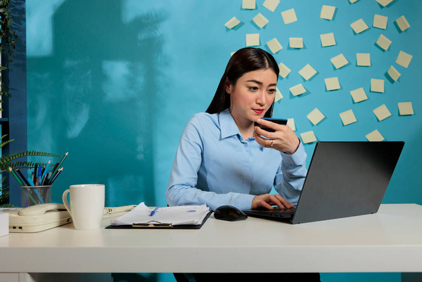 Mujer profesional asiática sentada en el escritorio de la oficina haciendo compras en línea con el ordenador portátil. Empleada corporativa haciendo pagos de facturas en línea con tarjeta de crédito durante el día laboral. - Foto, Imagen