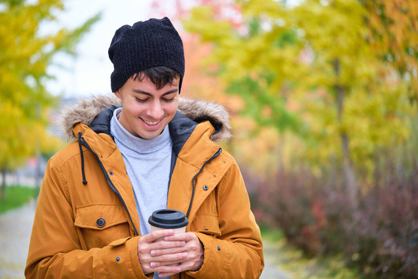 Усміхнений молодий чоловік тримає гарячу чашку кави в холодний осінній день
. - Фото, зображення