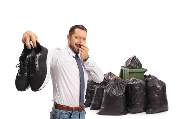 Man holding a pair of smelly trainers in front of waste bins isolated on white background - Φωτογραφία, εικόνα