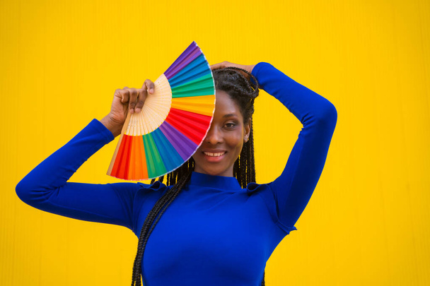A black ethnic woman with a rainbow lgbt fan on a yellow background - Foto, Imagem