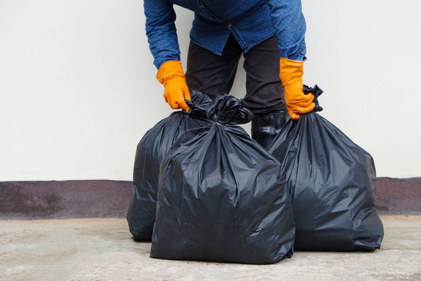 Yakındaki adam içinde çöp olan siyah plastik torbayı tutuyor. Konsept, atık yönetimi. Çevre sorunları. Günlük ev işleri. Çöpleri at. Çöp tasnif etme.      - Fotoğraf, Görsel
