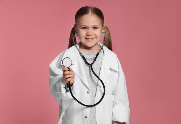 Pembe arka planda steteskobu olan tıp üniformalı küçük bir kız. - Fotoğraf, Görsel
