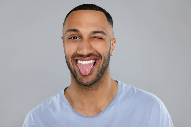 Happy young man showing his tongue on light grey background - Foto, immagini