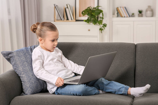 Little girl using laptop on sofa at home. Internet addiction - Foto, afbeelding