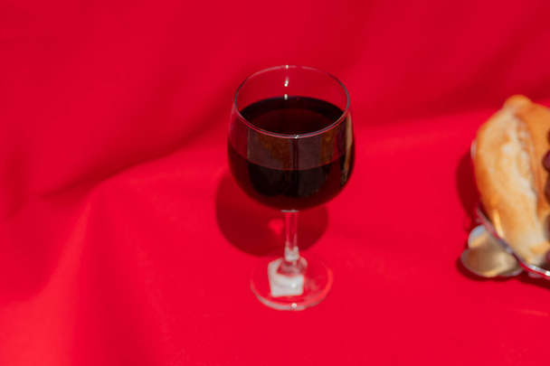 Wine glass, bread and grapes on red cloth in hard light. Symbolism of the last supper of Christ Jesus - Photo, Image